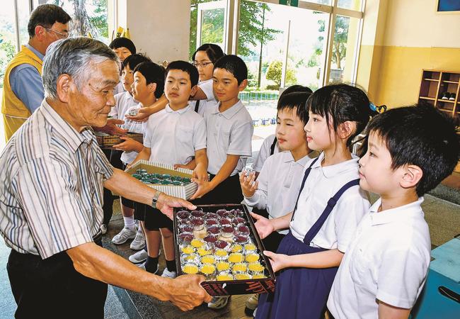 手作りのろうそくを松本広志さん（左手前）らに手渡す児童＝雲南市大東町北村、海潮小学校