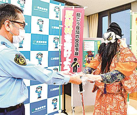 柿丸道生署長（左）から夜光反射材を受け取る倭川戸神楽社中の団員＝江津市江津町、江津署