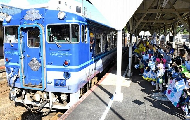 小旗を振って観光列車「あめつち」を見送る園児ら＝雲南市木次町里方、木次駅
