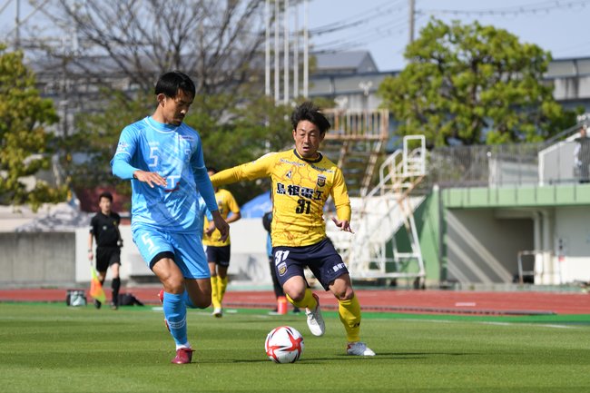 前半、今季初スタメンのＦＣ神楽しまねＭＦ田平謙（右）がドリブルで攻め込む＝枚方市立陸上競技場