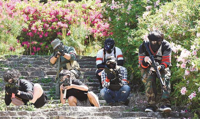 草むらに隠れたり、姿勢を低くしたりして敵チームと撃ち合う参加者＝松江市宍道町白石、宍道総合公園古墳の森