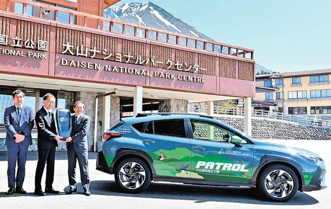 鳥居敏夫専務理事（右）にビッグキーを手渡す鈴木泰介社長（中央）＝鳥取県大山町大山、大山ナショナルパークセンター