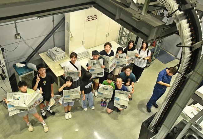 刷り上がった新聞を手に輪転機を見学する参加者=出雲市斐川町上庄原、山陰中央新報製作センター
