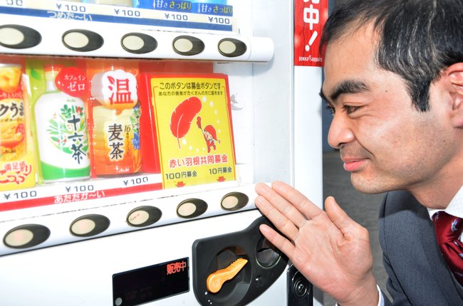 募金ボタンがある自動販売機を紹介する庄司慎平社長＝境港市渡町