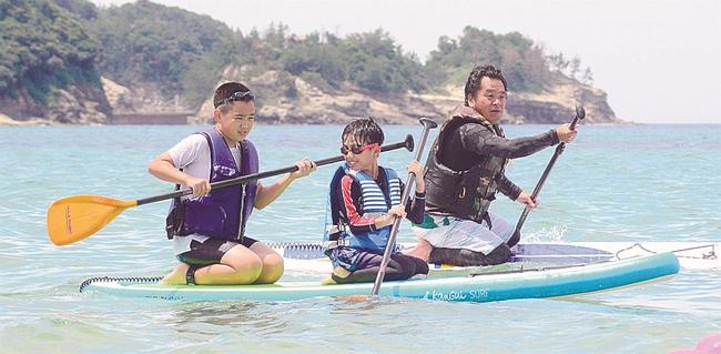 ボードに座ってパドルをこぐ参加者=大田市仁摩町馬路、琴ケ浜
