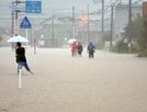 道路が冠水し、膝下まで水につかりながら歩く住民＝１３日午前１０時４１分、鳥取市福部町