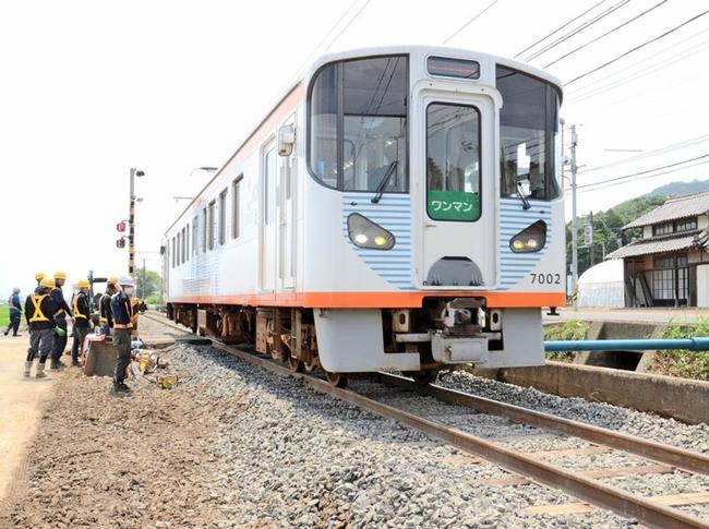 不通となっていた区間の補修作業を行う作業員の横を通過する一畑電車=出雲市美談町