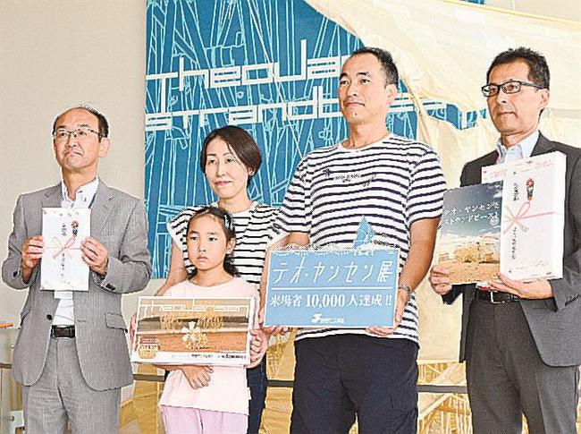 来場１万人目となり展示作品をバックに記念撮影する藤田守彦さん（右から２人目）ら＝松江市袖師町、島根県立美術館