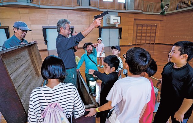 箱の中に隠れていた大人を見つける児童たち＝島根県美郷町都賀西、大和小学校体育館