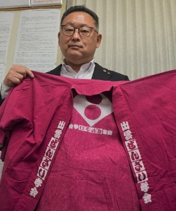 現地で着る「出雲ぜんざい学会」の法被を手にPRへ意気込む渡部稔会長=出雲市大社町北荒木、出雲観光タクシー