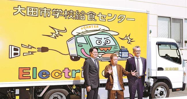 「バキバキ画」が描かれた給食運搬用のＥＶトラックの前でポーズを取るネゴシックスさん（中央）＝大田市川合町、市学校給食センター