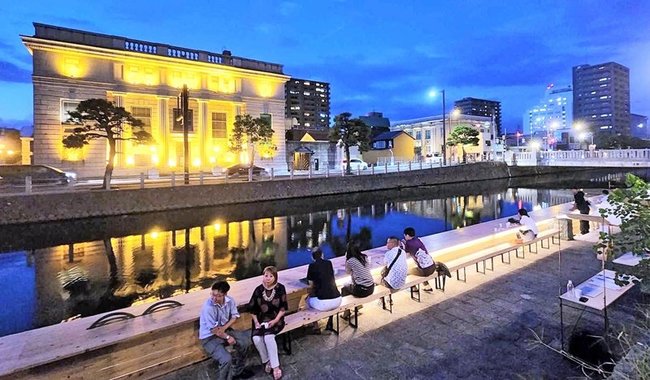 ライトアップされた京橋川沿いのテラスでくつろぐ観光客（２０２３年撮影）