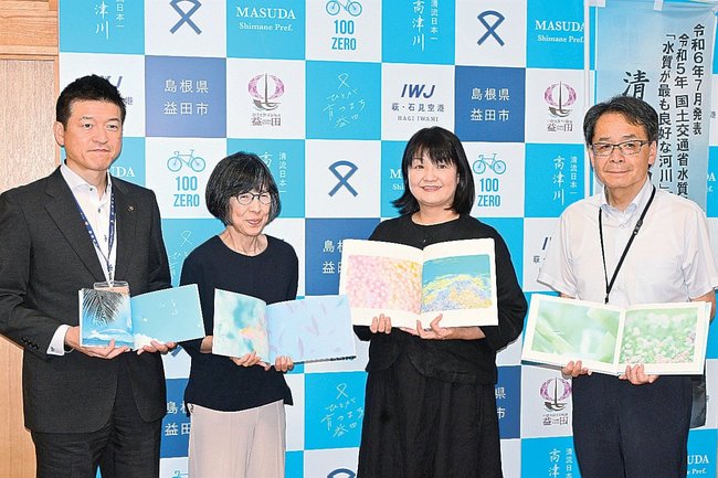 寄贈した写真集を広げる「ふぉとみ」の友重明美代表（左から３人目）ら関係者たち＝益田市常盤町、市役所