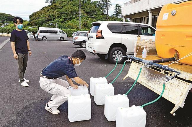 給水所に持ち込まれたポリタンクに水を注ぐ出雲市職員（手前）＝１９日午前１１時３分、出雲市多伎町小田、市多伎行政センター