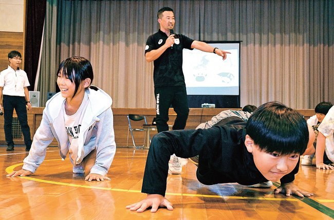 山本隼年さん（中央）が紹介する運動を体験する児童たち＝出雲市佐田町須佐、須佐小学校