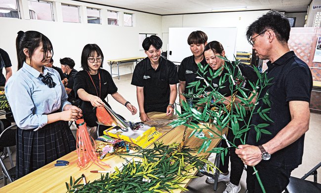 三好正師会長(右)に教わりながら七夕飾りを作る島根フィルティーズの選手や島根中央高校生ら=島根県川本町川本、中新町自治会館