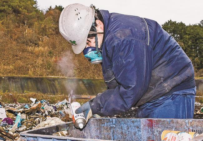 スプレー缶のガス抜きをする作業員＝松江市西持田町、不燃物処理場