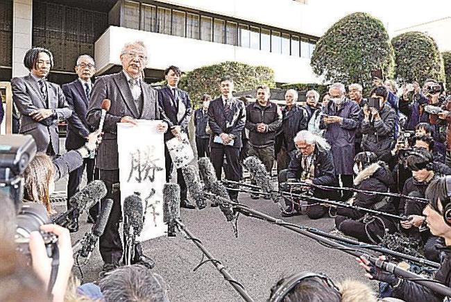 起訴取り消しを巡る損害賠償訴訟の判決を終え、「勝訴」の紙を手に取材に応じる「大川原化工機」の大川原正明社長（左から３人目）＝２７日午後、東京地裁前
