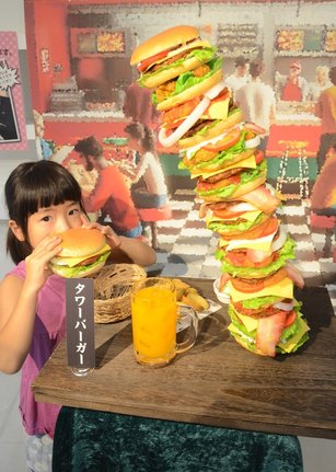 今にも倒れそうな「タワーバーガー」と記念撮影用のバーガーを手にする子ども＝倉吉市鍛冶町１丁目、円形劇場くらよしフィギュアミュージアム