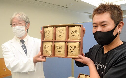 贈呈式で、パッケージに「感謝」と書いたコーヒーを掲げる小阪真二病院長（左）と門脇裕二代表＝出雲市姫原４丁目、島根県立中央病院