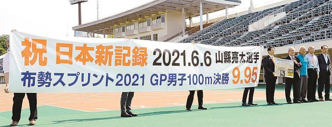 横断幕を掲げ、日本記録樹立を祝う陸上競技関係者＝鳥取市布勢、ヤマタスポーツパーク陸上競技場