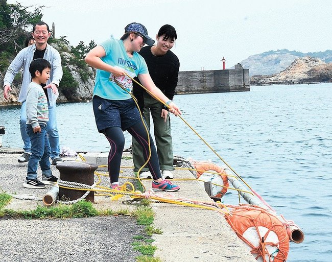 岸壁からコンクリートブロックの付いたロープを引き上げる選手＝出雲市大社町宇龍