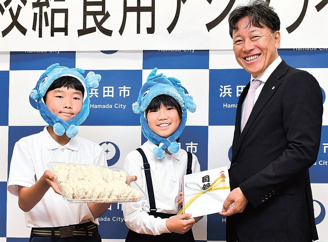 児童にアジフライの目録を手渡す高橋利明社長（右）＝浜田市下府町、国府小学校