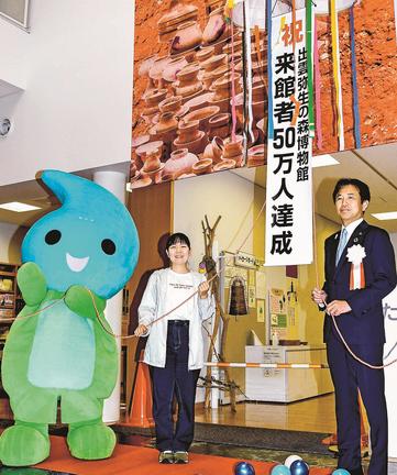 ５０万人目となりくす玉を割る笠川佳奈さん（中央）＝出雲市大津町、出雲弥生の森博物館