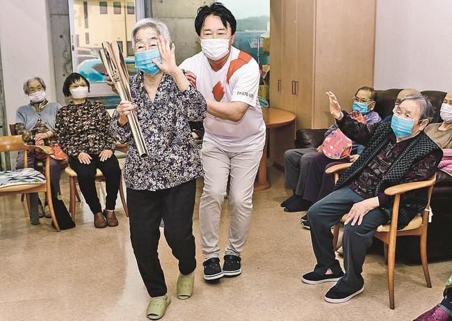 トーチを手にして歩く入所者の肩を支える斉藤憲嗣さん＝江津市和木町、よろこぼう屋マンション