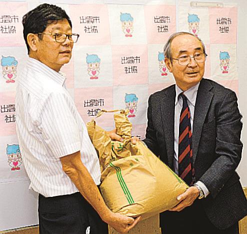 出雲市社会福祉協議会の渡部英二会長(右)に食料品を手渡す、報雲会の勝部径司会長=雲市今市町、市社会福祉センター