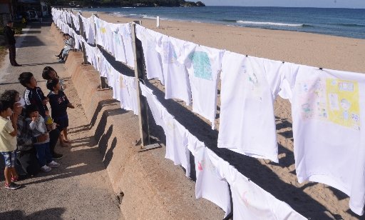 浜辺に並ぶＴシャツを眺める地元住民＝大田市仁摩町馬路、琴ケ浜