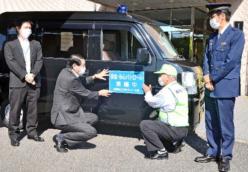 青色回転灯付きの公用車にシートを張る清原正義学長（左から２人目）ら＝浜田市野原町、島根県立大浜田キャンパス