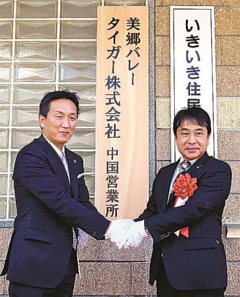 看板を除幕し、握手する嘉戸隆町長（右）と尾田英登社長＝島根県美郷町粕渕
