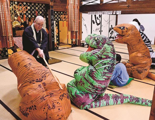 恐竜になりきって座禅を体験し、醍醐靖幸住職から警策を受ける参加者=安来市清井町、雲樹寺