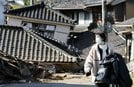 地震で倒壊した建物の前を歩く女性＝２日午前１１時２８分、石川県能登町