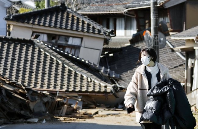 地震で倒壊した建物の前を歩く女性＝２日午前１１時２８分、石川県能登町