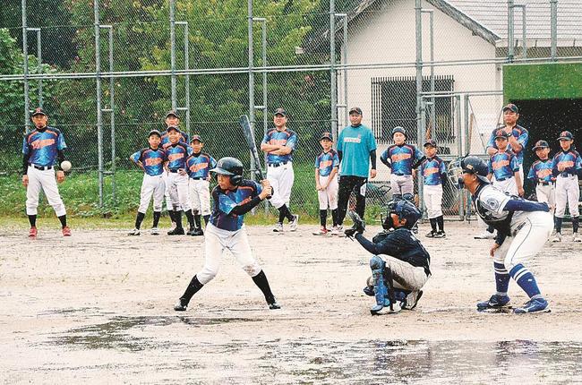 土砂降りの中、交流試合をする少年野球チームの選手たち＝島根県西ノ島町美田、西ノ島総合公園野球場