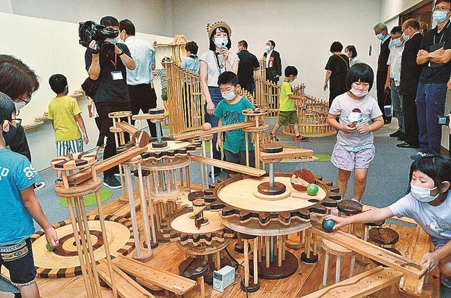 地元産材を使った新作「歯車の遊園地」で遊ぶ保育園児と、つちやあゆみさん（中央）＝鳥取県日南町霞、町美術館