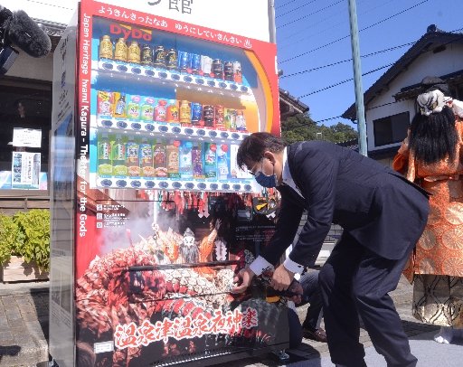 夜神楽をデザインした自動販売機で商品を買う関係者＝大田市温泉津町温泉津、ゆうゆう館前