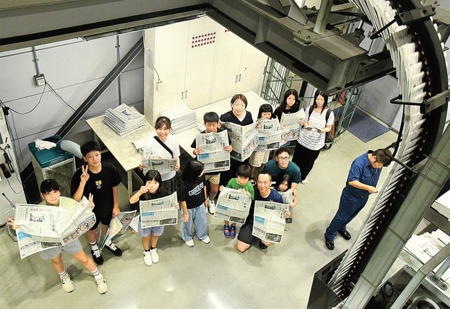 刷り上がった新聞を手に輪転機を見学する参加者＝出雲市斐川町上庄原、山陰中央新報製作センター