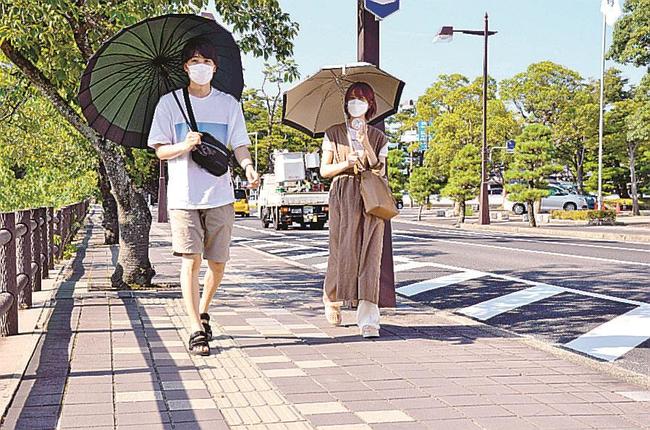 強い日差しが照りつける中、日傘を差して歩く観光客＝４日午後４時３分、松江市殿町