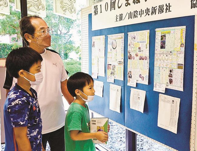 出雲市内の小中学生が制作した新聞に見入る来館者＝出雲市大津町、出雲中央図書館