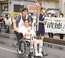 沿道の施設職員たちの応援を受けながら、聖火をつなぐ永間清徳さん＝島根県川本町川本