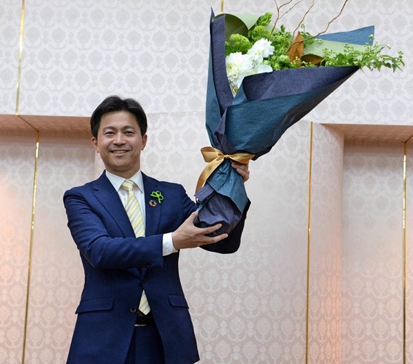 当選確実の報を受け、花束を掲げて喜ぶ上定昭仁氏＝18日午後８時55分、松江市殿町、サンラポーむらくも