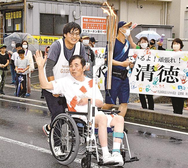沿道の施設職員たちの応援を受けながら、聖火をつなぐ永間清徳さん＝島根県川本町川本