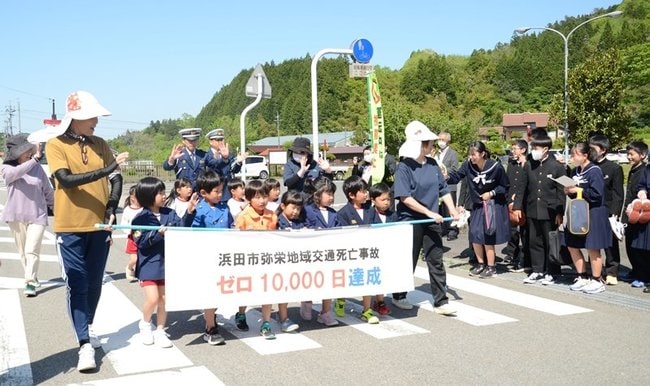 交通死亡事故ゼロ１万日達成の横断幕を持って大通りを歩く園児たち＝浜田市弥栄町長安本郷