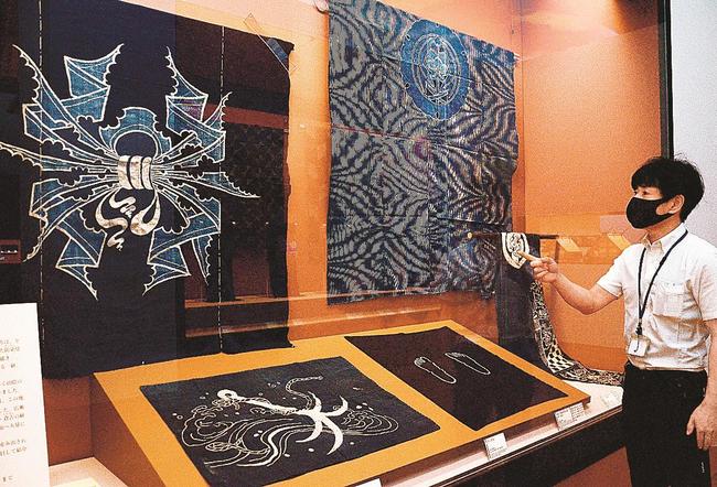 熨斗を描いた風呂敷（左上）など大胆でユニークな柄があしらわれた筒描きを紹介する岡宏三専門学芸員＝出雲市大社町杵築東、島根県立古代出雲歴史博物館