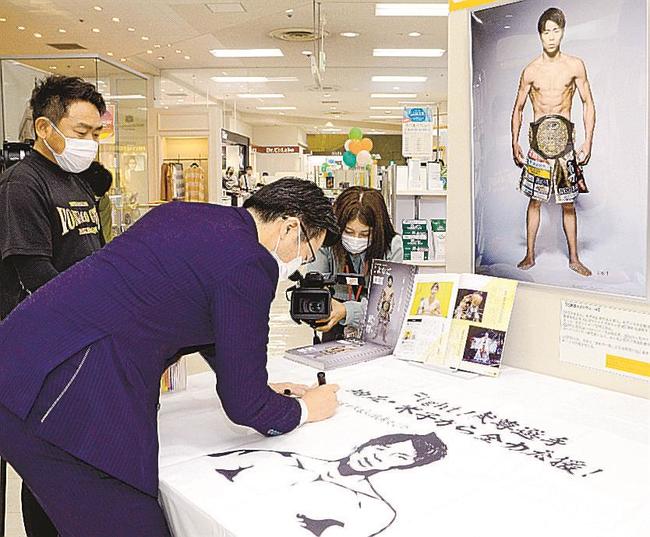 武尊選手の写真を前に、応援メッセージを書き入れる伊木隆司市長と、米子ジムの富村誠司代表＝米子市角盤町１丁目、ＪＵ米子高島屋