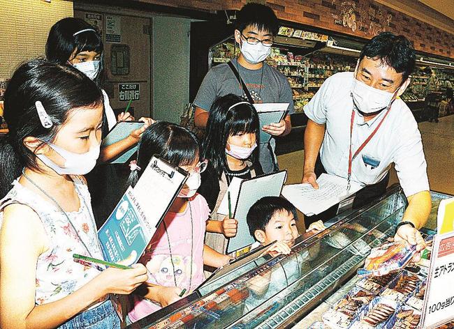 魚売り場で環境を守る基準に合格した商品について売り場の担当者（右）に取材する子ども記者たち＝松江市東朝日町、イオンスタイル松江