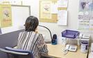 「いのちの電話」の電話相談を受けるデスクに座るスタッフの女性